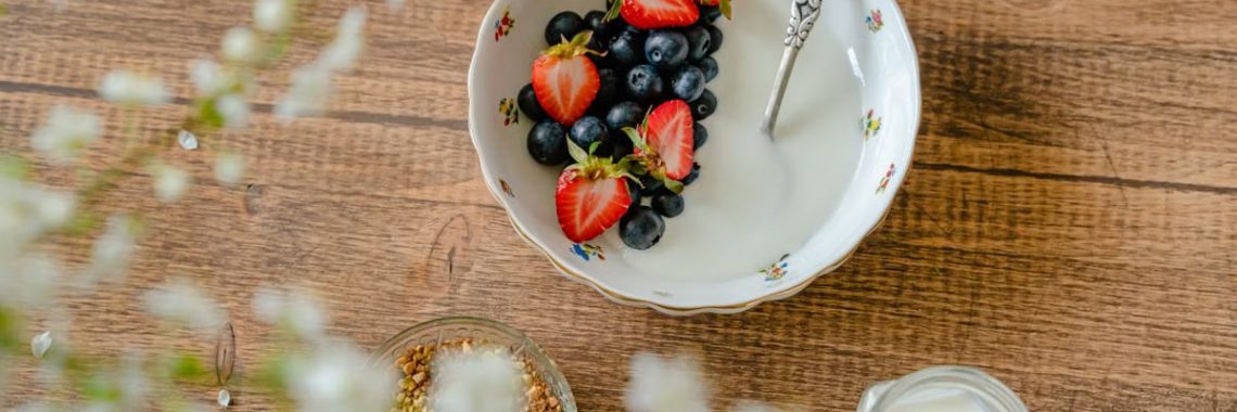 A bowl of fresh strawberries, blueberries with yogurt on a wooden table, viewed from above.